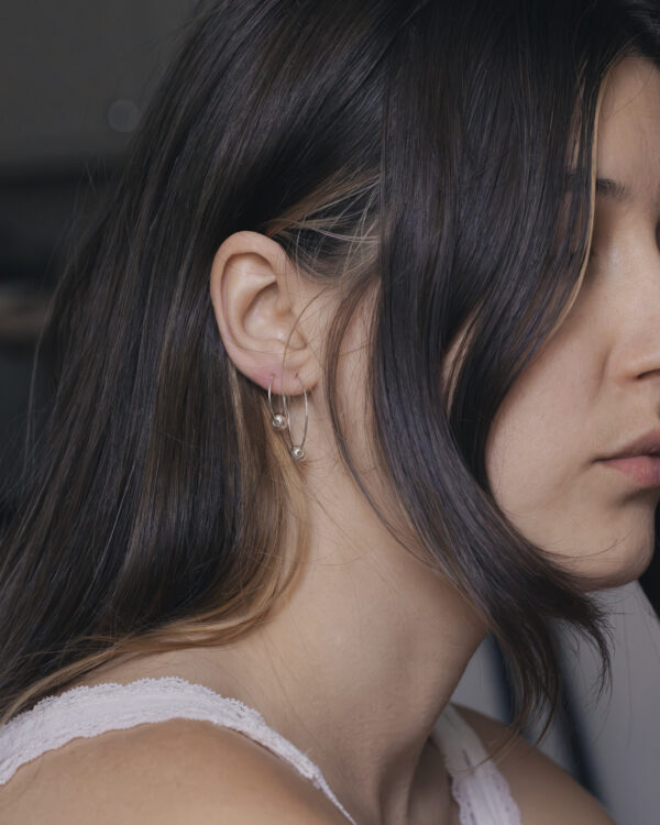 close up side view of a woman with two silver bauble hoops in one ear
