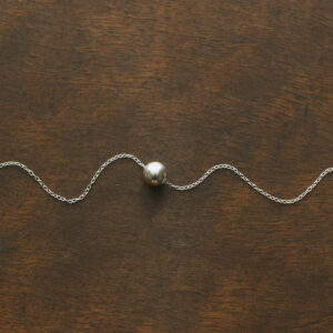 bauble necklace laid out with the chain in a squiggle shape on a wooden surface