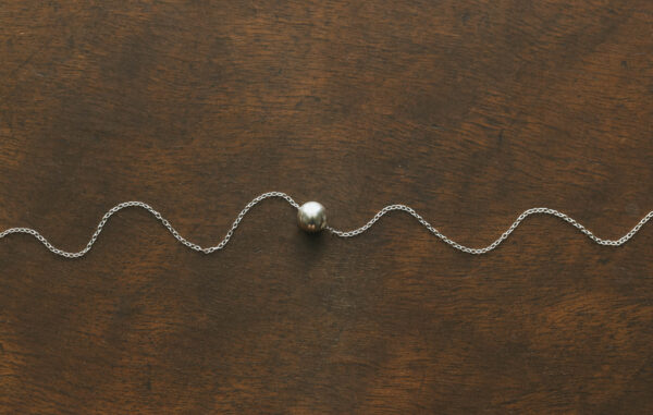 bauble necklace laid out with the chain in a squiggle shape on a wooden surface