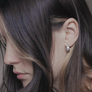 Side view of a womans faec showing off silver hoop earring, hair tucked behind ear with strands covering face
