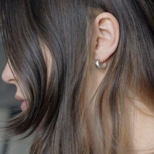 Close-up of a womans ear in side profile, Showing a silver chunky hoop with brown hair arranged around the face