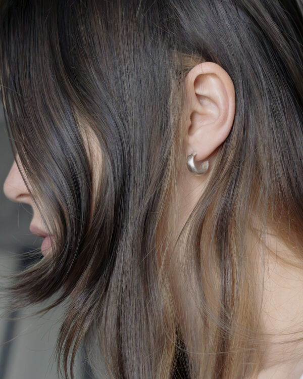 Close-up of a womans ear in side profile, Showing a silver chunky hoop with brown hair arranged around the face