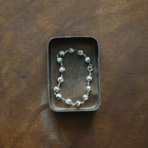 beaded bracelet displayed in a metal tin on a wooden surface
