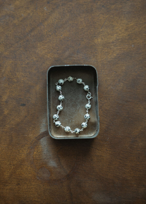 beaded bracelet displayed in a metal tin on a wooden surface