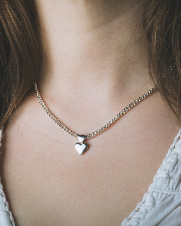 close up of a silver heart necklace on womans neck